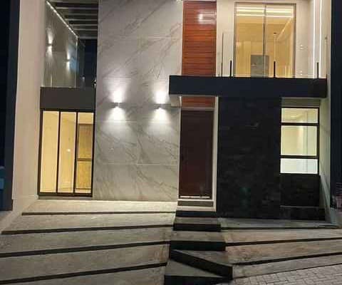 Foto noturna de residência entregue — fachada com mármore, ripado e iluminação cênica